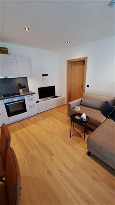 Eine moderne Wohnung mit einer offenen Küche und einem gemütlichen Wohnbereich. Der Boden ist aus Holz und die Einrichtung ist schlicht und einladend.