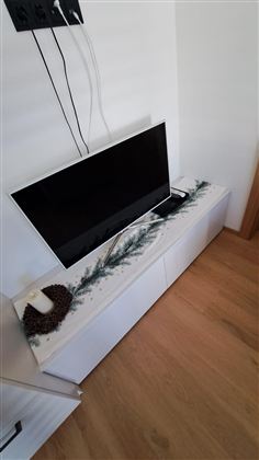 Ein moderner Fernseher steht auf einem weißen TV-Schrank. Der Schrank hat eine hübsche Dekoration aus Holz und Pflanzen.