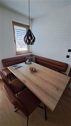 Ein gemütlicher Essbereich mit einem Holztisch und braunen Sitzbänken. Auf dem Tisch stehen eine Schale mit Früchten und eine Zeitschrift.