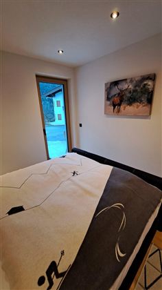 Ein gemütliches Schlafzimmer mit einem großen Bett und einer modernen Einrichtung. Durch das Fenster ist ein schöner Ausblick auf die Natur sichtbar.