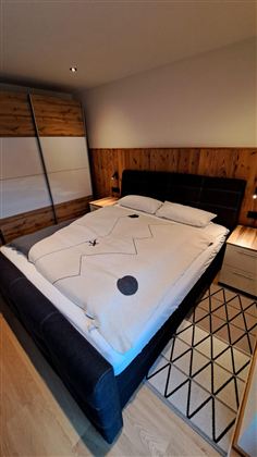 Ein modernes Schlafzimmer mit einem großen Bett und Holzwänden. Auf dem Boden liegt ein Teppich mit geometrischem Muster.