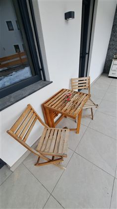 Ein kleiner Balkon mit zwei alten Holzstühlen und einem passenden Tisch. Der Tisch hat eine Pflanze darauf und der Boden ist gefliest.