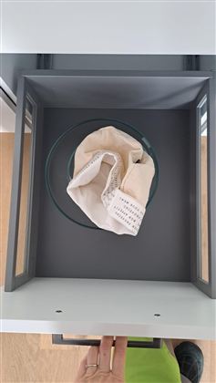 Eine offene Schublade mit einer Glasschale und einem Stoffbeutel. Der Innenraum ist grau und hell beleuchtet.