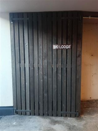 Ein Holzschiebetor mit der Aufschrift "SKI LODGE". Die Tür ist in einem modernen, rustikalen Stil gehalten.