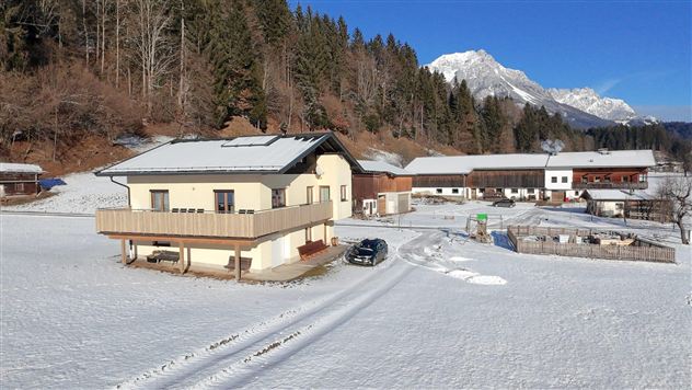Een modern huis in een besneeuwd landschap. Op de achtergrond zijn bergen en bomen te zien.