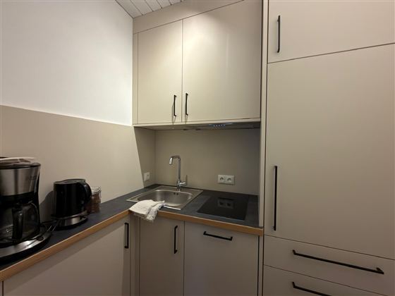 Een moderne keukenoek met grijze kasten en een praktische gootsteen. Ook te zien zijn een koffiezetapparaat en keukenapparaten.