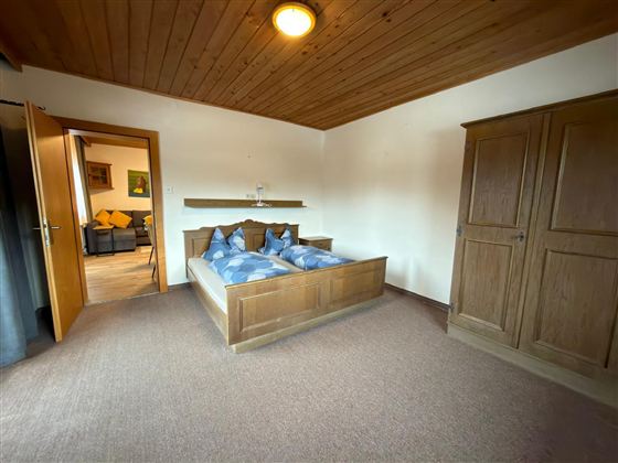 Een gezellige slaapkamer met een tweepersoonsbed en blauwe kussens. Op de achtergrond is een kast en een open deur naar een andere ruimte te zien.