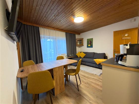 Een gezellige woonkamer met een eethoek en een bank. Grote ramen zorgen voor veel daglicht.