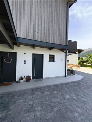 Ein modernes Haus mit Holzverkleidung und zwei Eingängen. Der gepflasterte Weg führt zur Terrasse und in den Garten.
