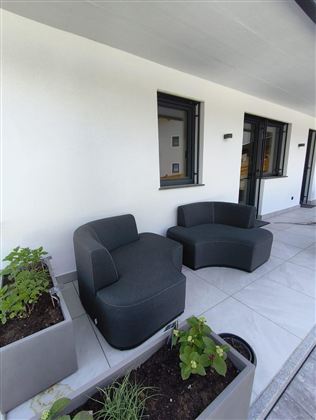 Eine moderne Terrasse mit zwei eleganten, grauen Sitzmöbeln. Im Hintergrund sind Fenster und Pflanzenkästen zu sehen.
