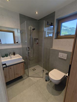 Ein modernes Badezimmer mit einer bodengleichen Dusche und einem Waschbecken. Große Fenster sorgen für viel Tageslicht und eine angenehme Atmosphäre.