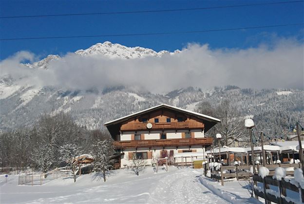 A picturesque chalet in the snowy landscape, surrounded by mountains. The sky is blue and sunny, creating a winter idyll.
