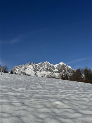 A snow-covered landscape with high mountains in the background. The sky is clear and blue.