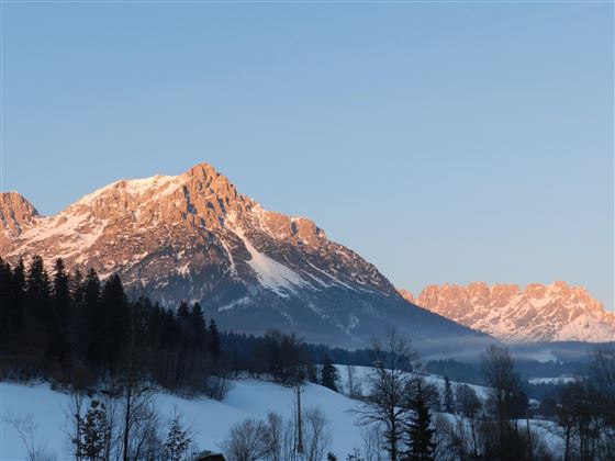 Eine beeindruckende Berglandschaft mit schneebedeckten Gipfeln und klarem Himmel. Die Sonne beleuchtet die Berge und schafft eine malerische Atmosphäre.