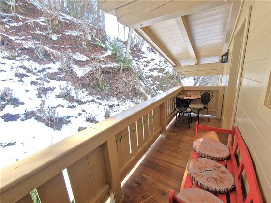 A cozy balcony with a red seating area and a small table. In the background, snow-covered mountains are visible.