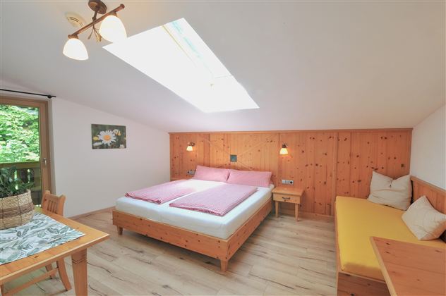 A cozy room with a double bed and a seating area. The walls are made of wood and a skylight provides plenty of daylight.