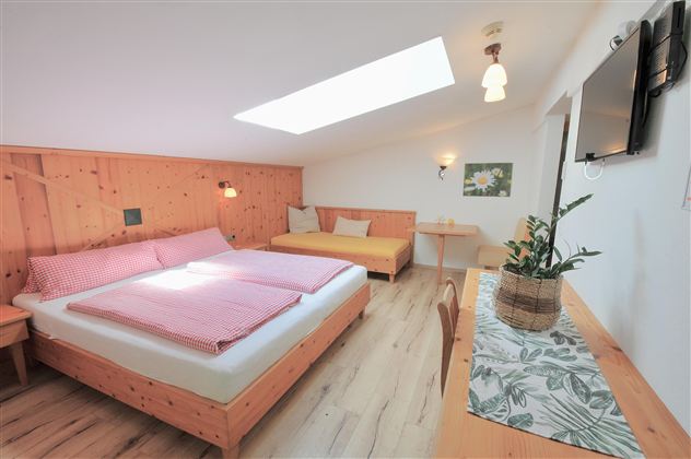 A cozy bedroom with a double bed and a sofa bed. The room has bright walls, wooden paneling, and plenty of natural light.