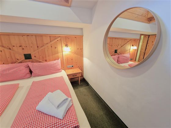 A cozy bedroom with a double bed and checked bedding in red. The round mirror and wooden walls create a warm atmosphere.