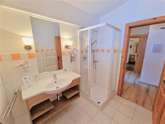 A modern bathroom with a shower cubicle and a sink. The walls are tiled in light colors and there are wood details in the room.
