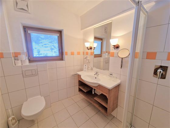 A modern bathroom with a shower, sink, and mirror. The walls are brightly tiled, and there is a window that lets in daylight.