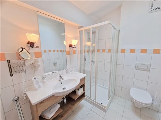A modern bathroom with a shower, sink, and toilet. It is bright and friendly with tiles in white and orange.