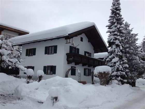 A cozy house in the snow with a beautiful balcony.  
Surrounded by snow-covered trees and a wintry landscape.