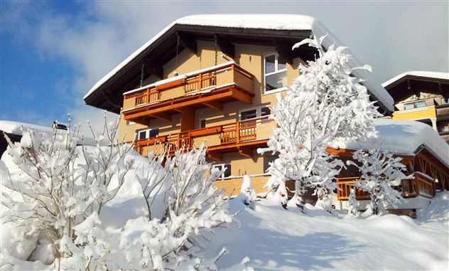 A charming house in the snow with wooden decorations and balconies. The surroundings are characterized by white snow and snow-covered trees.