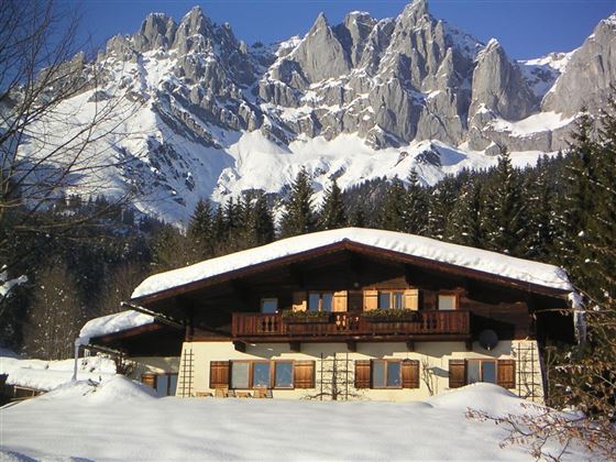 A charming house in the snow with a snow-covered roof. Majestic mountains rise in the background.