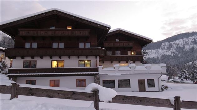 A cozy chalet in the snow with a warm light coming from the windows. Snow-covered mountains are visible in the background.