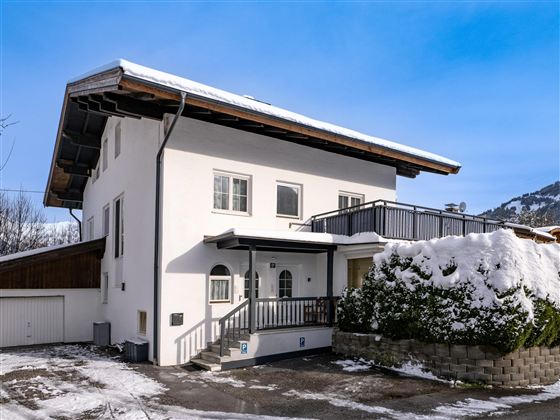 A modern house with a white facade and a balcony. The winter has covered the surroundings with snow.