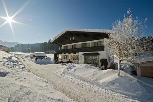 Ein gemütliches Haus im Schnee mit einem klaren blauen Himmel. Die Sonne strahlt über die Winterlandschaft.