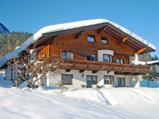 Ein charmantes Holzhaus im Schnee mit einem großen Dach. Die Umgebung ist winterlich mit frischem weißem Schnee.