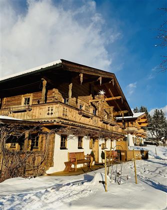 A traditional wooden house in the snow with a large balcony. The sky is clear and the surroundings exude a wintry calm.