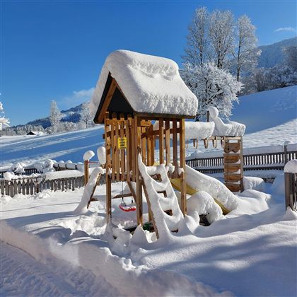 A playground in winter, covered with snow. The structures are hidden under a thick layer of snow and the landscape is snowy.