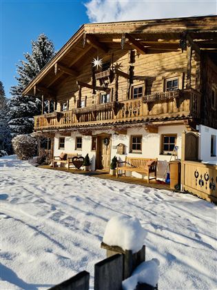 A traditional wooden house in the snow with a cozy balcony. The surroundings are wintry and peaceful.