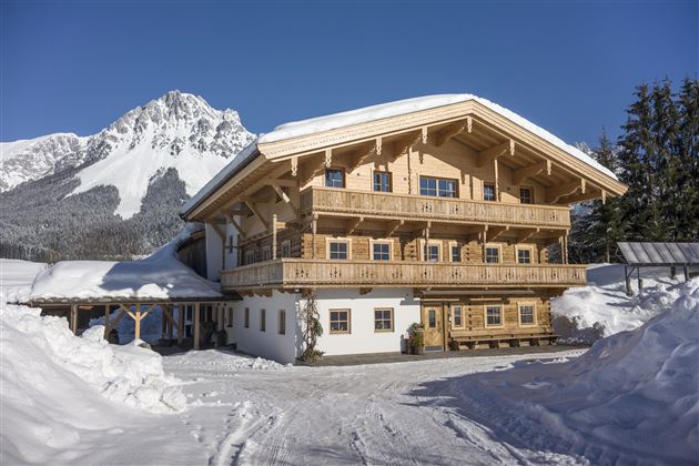 A cozy wooden house in the snow with a beautiful mountain in the background. The sunny winter landscape radiates peace and idyllic charm.