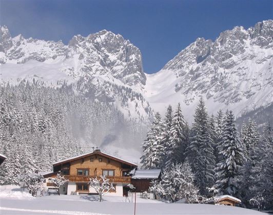 A picturesque chalet in a snowy winter landscape. High mountains and dense forests surround the scene.