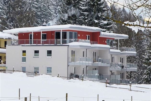A modern building in the snow with red and white elements. Snow-covered trees are visible all around.