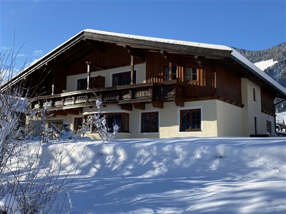 Ein gemütliches Holzhaus in einer verschneiten Landschaft. Der klare blaue Himmel ergänzt die Winteridylle.