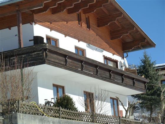 A traditional house in alpine style with wood embellishments. The clear sky and the adjacent trees create a tranquil atmosphere.