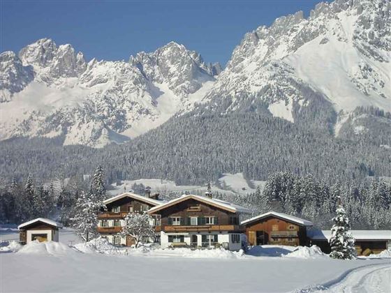 A picturesque alpine landscape with snow-covered mountains in the background. In front stands a cozy wooden house, surrounded by smooth, white snow.