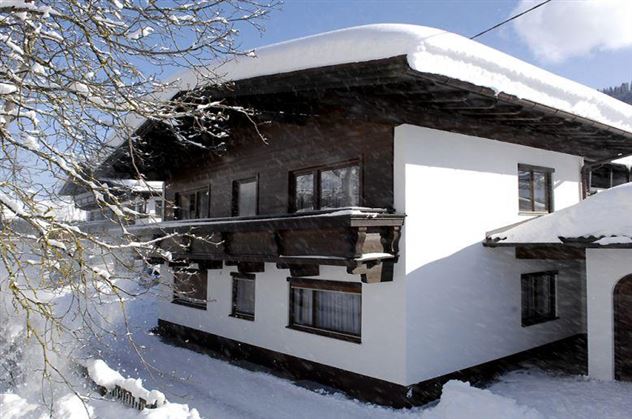 A cozy house in the snow with a classic wooden roof. The surroundings are covered in fresh, white snow.