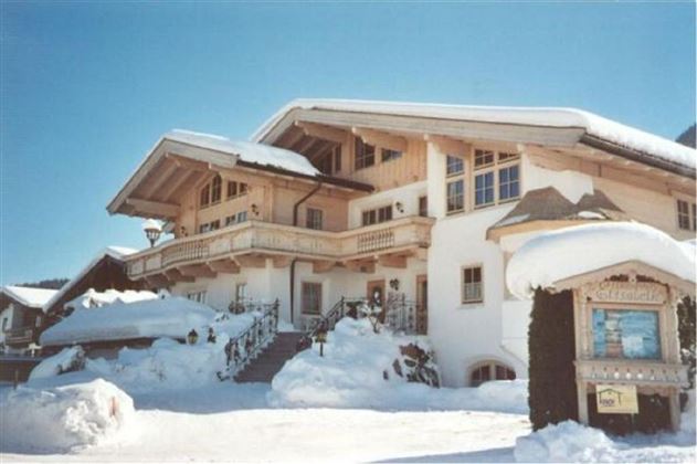 An elegant chalet in the snow with a spacious balcony. The entrance is surrounded by a picturesque snowy landscape.
