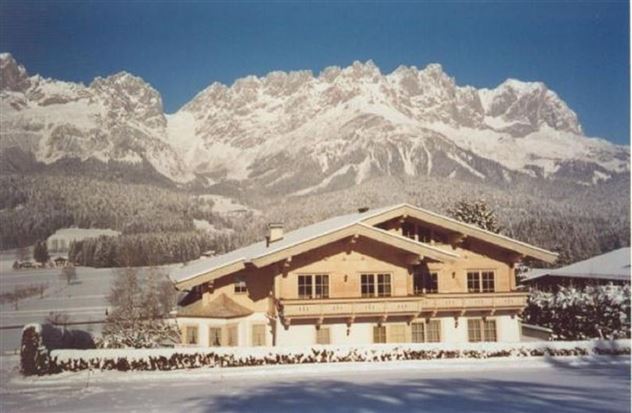 A charming wooden house in a snowy winter landscape. Majestic mountains rise in the background under a clear sky.