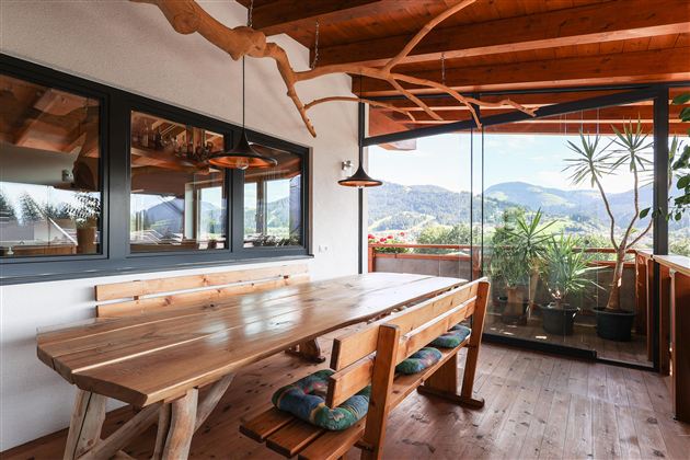 Ein gemütlicher Essbereich mit einem großen Holztisch und Bänken. Durch die Fenster sieht man die Berge und die Natur draußen.