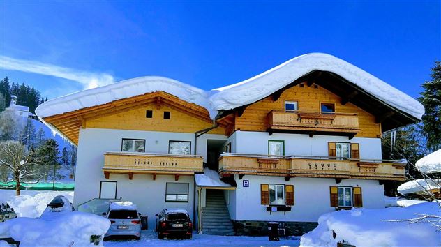 Ein charmantes Haus im alpenländischen Stil, bedeckt mit schneeigen Dächern. Die Umgebung ist winterlich und malerisch, ideal für winterliche Aktivitäten.