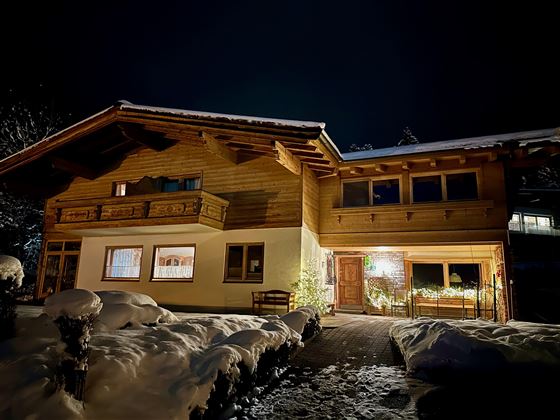 Ein gemütliches Holzhaus im Schnee bei Nacht. Die Fassade ist warm beleuchtet und schafft eine einladende Atmosphäre.