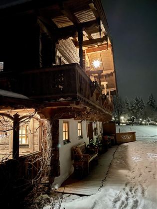 A cozy wooden house at night, illuminated by warm light. Surrounded by snow and a winter landscape.