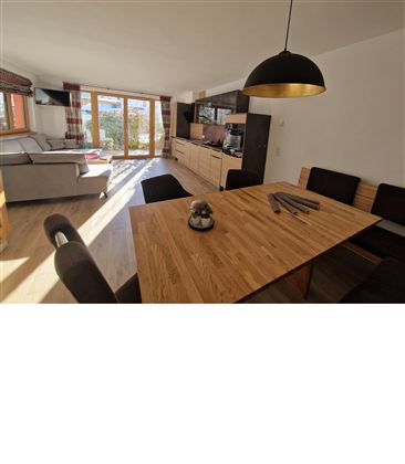 Ein helles und modernes Wohnzimmer mit großen Fenstern und Blick ins Freie. Ein stilvoller Esstisch aus Holz steht in der Mitte des Raums.