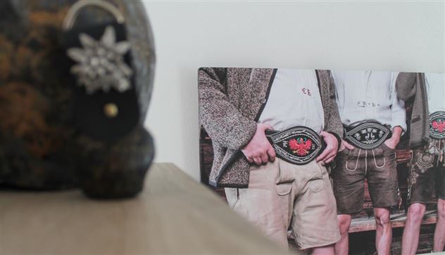 Eine Fotografie von drei Personen in traditioneller Kleidung, die jeweils einen Gurt mit einer großen Schnalle tragen. Im Vordergrund ist ein dekoratives Stück sichtbar.